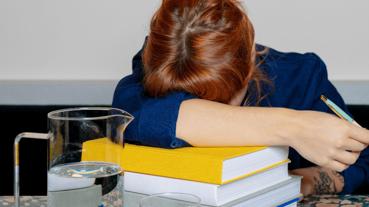 A stressed person rests their head on a pile of books, mulling over the difference between a consumer proposal vs debt consolidation and which would best suit their situation.