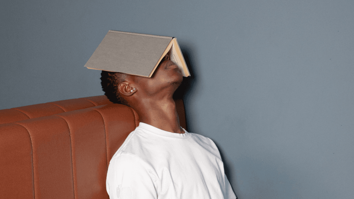 A stressed person leaning against a sofa with a book open on their face as they learn about the inconvenient truth of credit builder loans in Canada