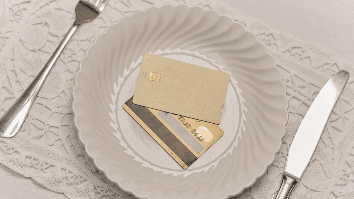 Two credit cards on a ceramic plate, between a set of utensils—a visual representation of the question: Does paying your credit card twice a month help with your credit score?