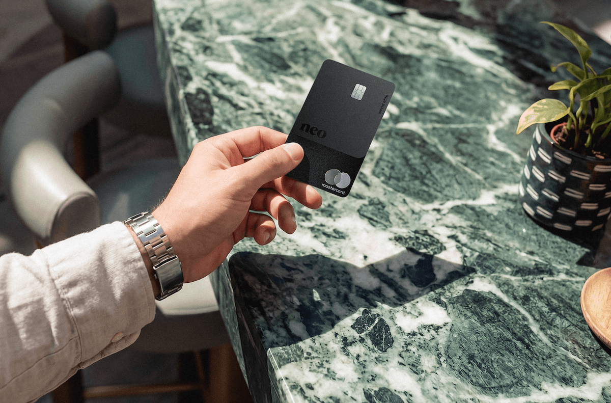 A person's hand holding the Neo World Elite Mastercard, a contender for one of the best cash back credit cards in Canada, over a marbled countertop