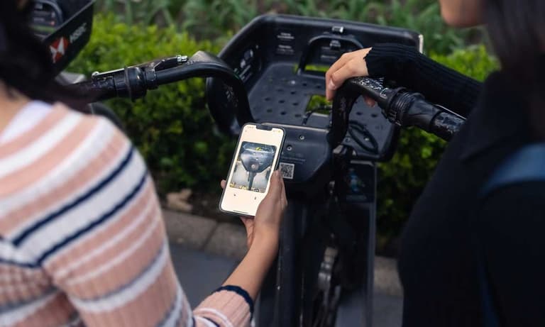 Two Canadian women taking a photo of a QR code to pay for a bike rental, but it could be a link to a phishing site for their credit card information.