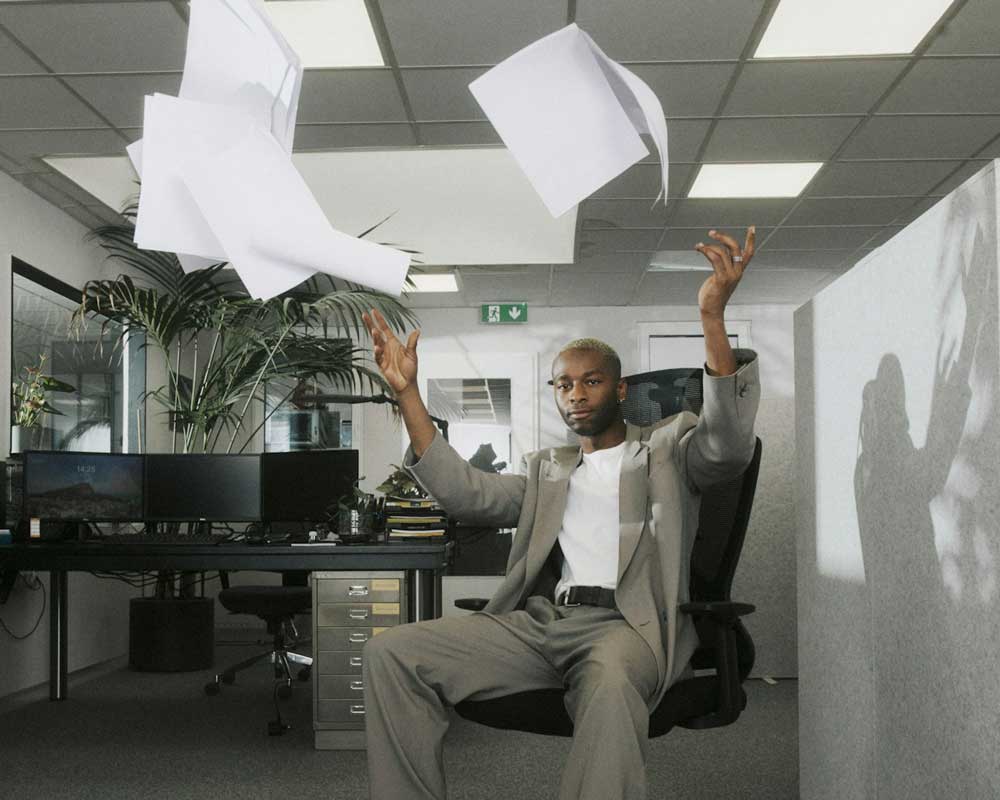 A Canadian man at his job, throwing paper up in the air, because he hasn’t been able to see his raise reflected in his paycheque.
